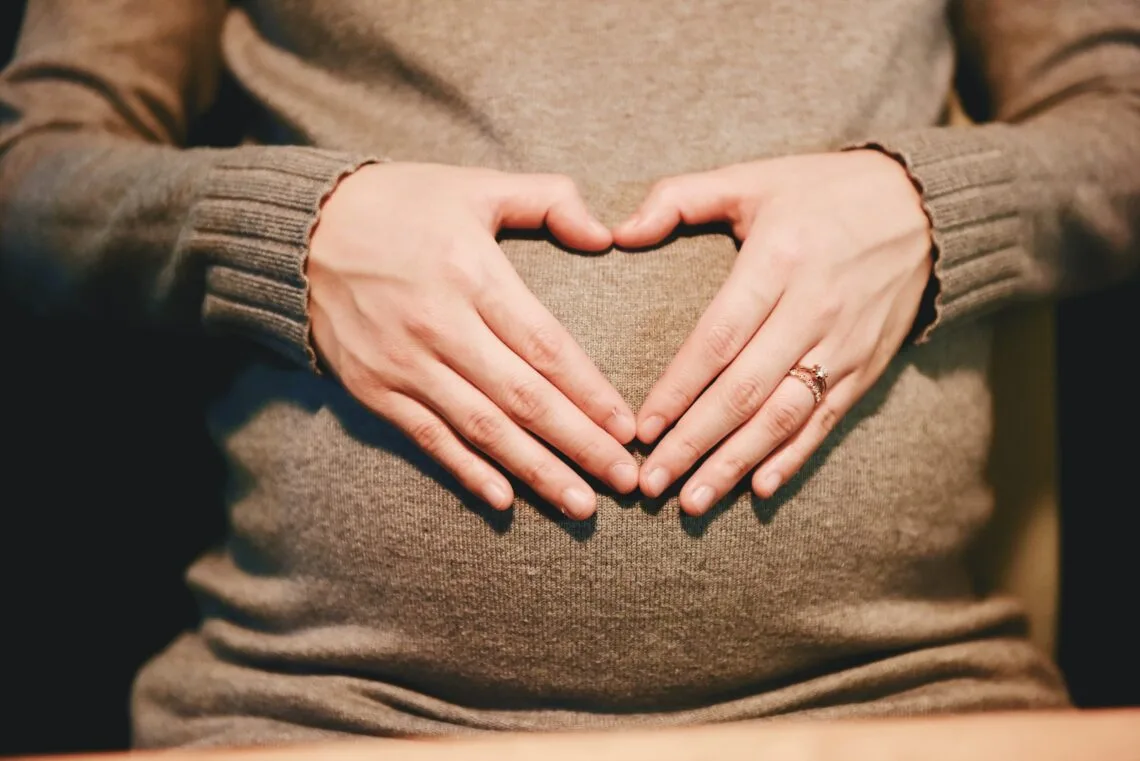 Pregnant woman forming a heart with her hands over her belly - pregnancy after a tummy tuck